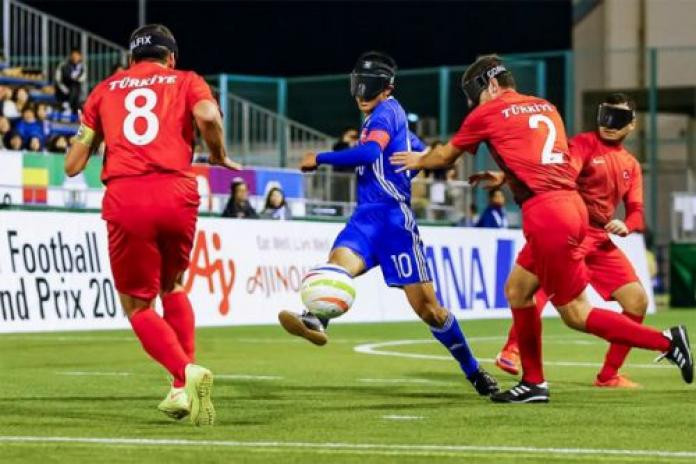 A Japanese blind footballer skillfully dribbles the ball past two defenders during a match