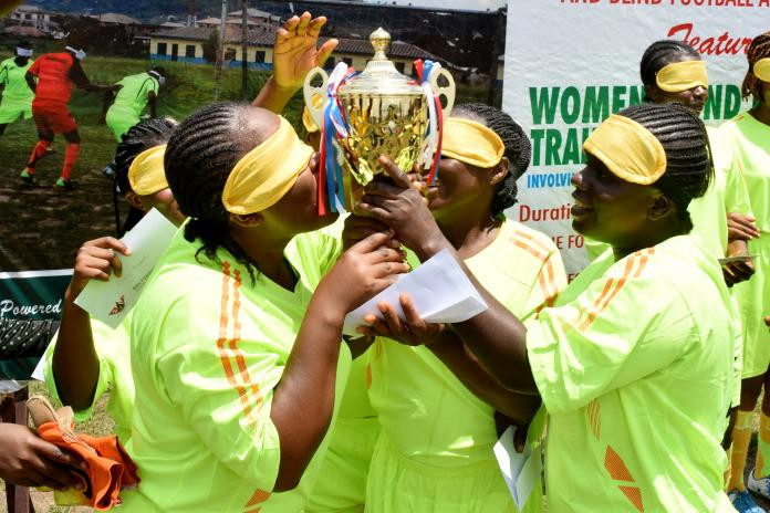 A team of four female blind footballers celebrating their victory with a trophy