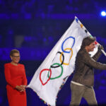 Tom Cruise holds the Olympic flag in front of Los Angeles Mayor Karen Bass as the flag is transferred to the next host city at the closing ceremony of the Paris 2024 Olympic Games.