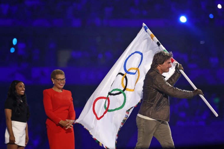 Tom Cruise holds the Olympic flag in front of Los Angeles Mayor Karen Bass as the flag is transferred to the next host city at the closing ceremony of the Paris 2024 Olympic Games.