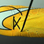 A yellow and orange Nike football boot featuring a white Swoosh and black laces.