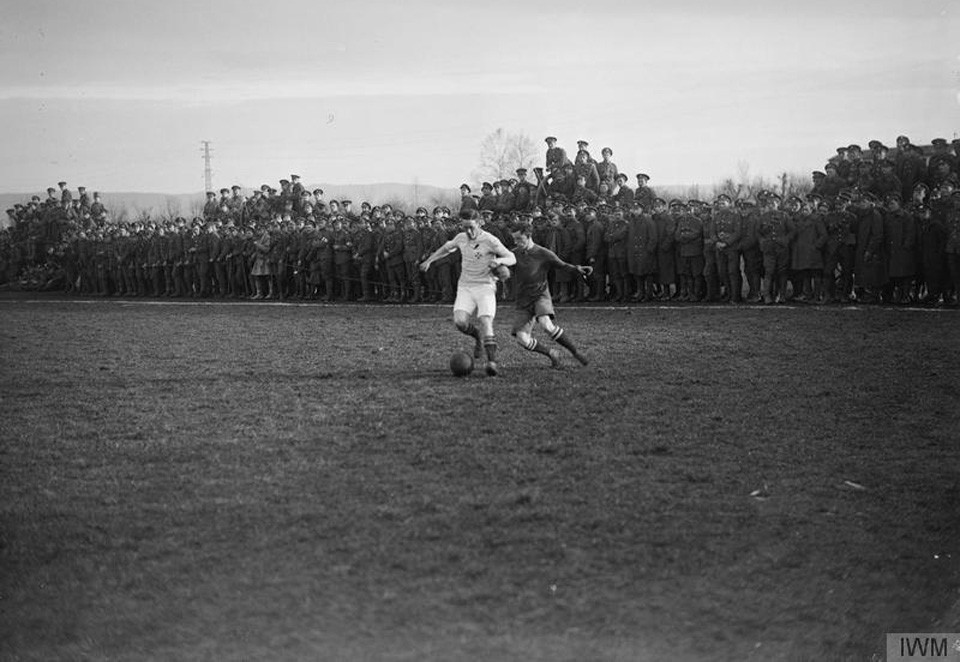 Final of the 48th Divisional Fanshawe Cup. The 1/7th Battalion Worcestershire Regiment versus 1/7th Battalion Royal Warwickshire Regiment. Two players tackle for the ball as soldiers scramble to get a view on the Italian Front, Trissino, Italy in 1918. Photo courtesy of Imperial War Museum