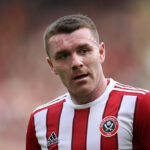 John Fleck played for Sheffield United in the Premier League, depicted in dynamic action, exemplifying the athleticism involved and the potential risks faced by professional soccer players.