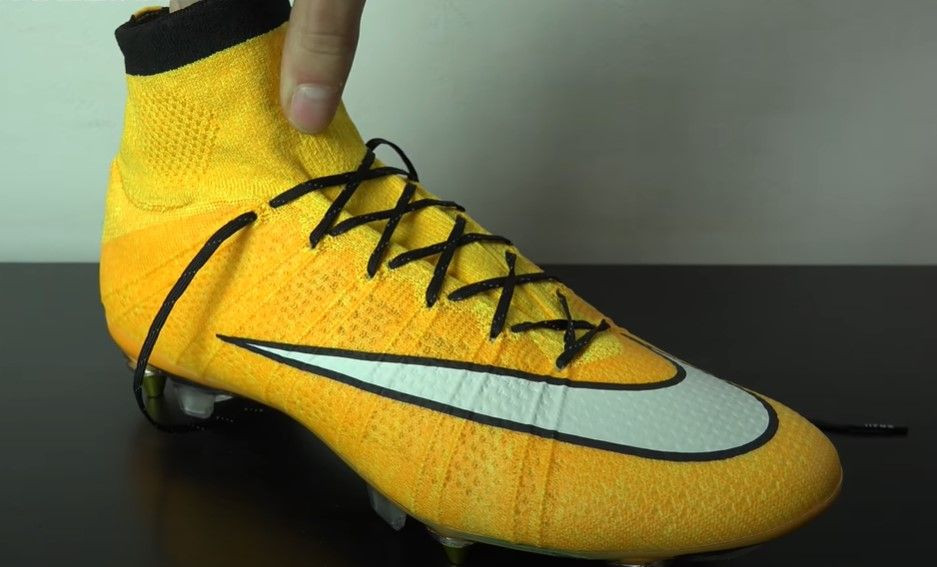 A yellow and orange Nike football boot featuring a white Swoosh and black laces.