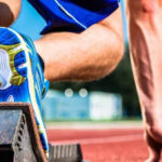 Close-up of an athlete in starting blocks on a track. The focus is on the runner