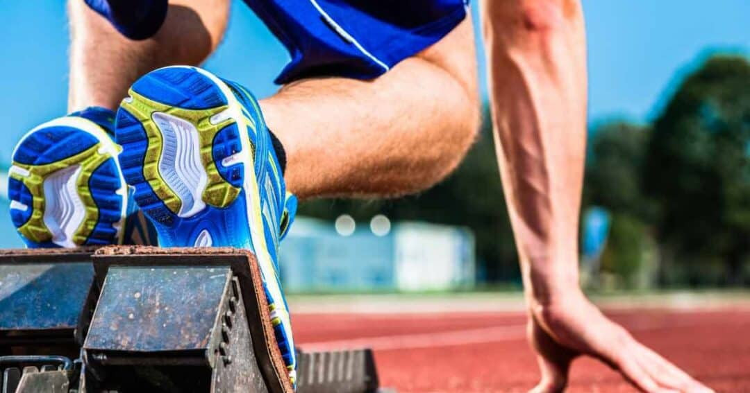Close-up of an athlete in starting blocks on a track. The focus is on the runner