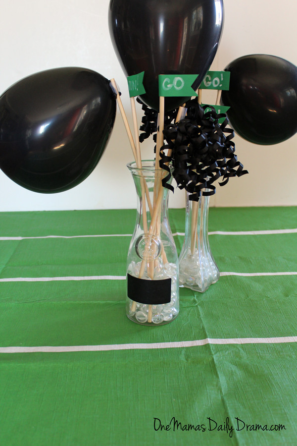 black balloons and streamers with green pennants in a glass vase for football party table decor