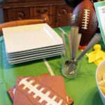 football napkins, silverware, and white square plates on a green football field tablecloth
