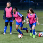 Girls playing football in a park, smiling and active.