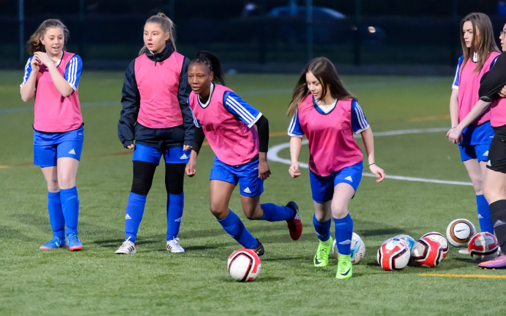 Girls playing football in a park, smiling and active.