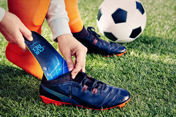 Person putting a blue insole for cleats into a soccer cleat