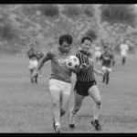 Black and white photograph of 2 soccer players kicking soccer ball