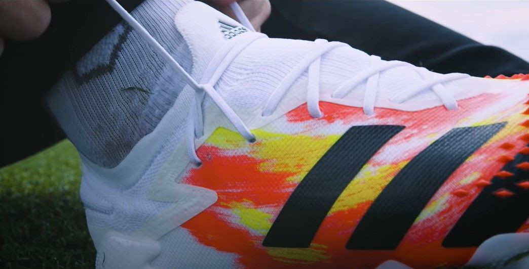 A white, orange, and yellow adidas football boot with a Runners Loop knot across the front.