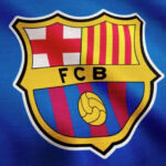 This image shows the iconic crest of FC Barcelona on a textured background that appears to be a section of the team