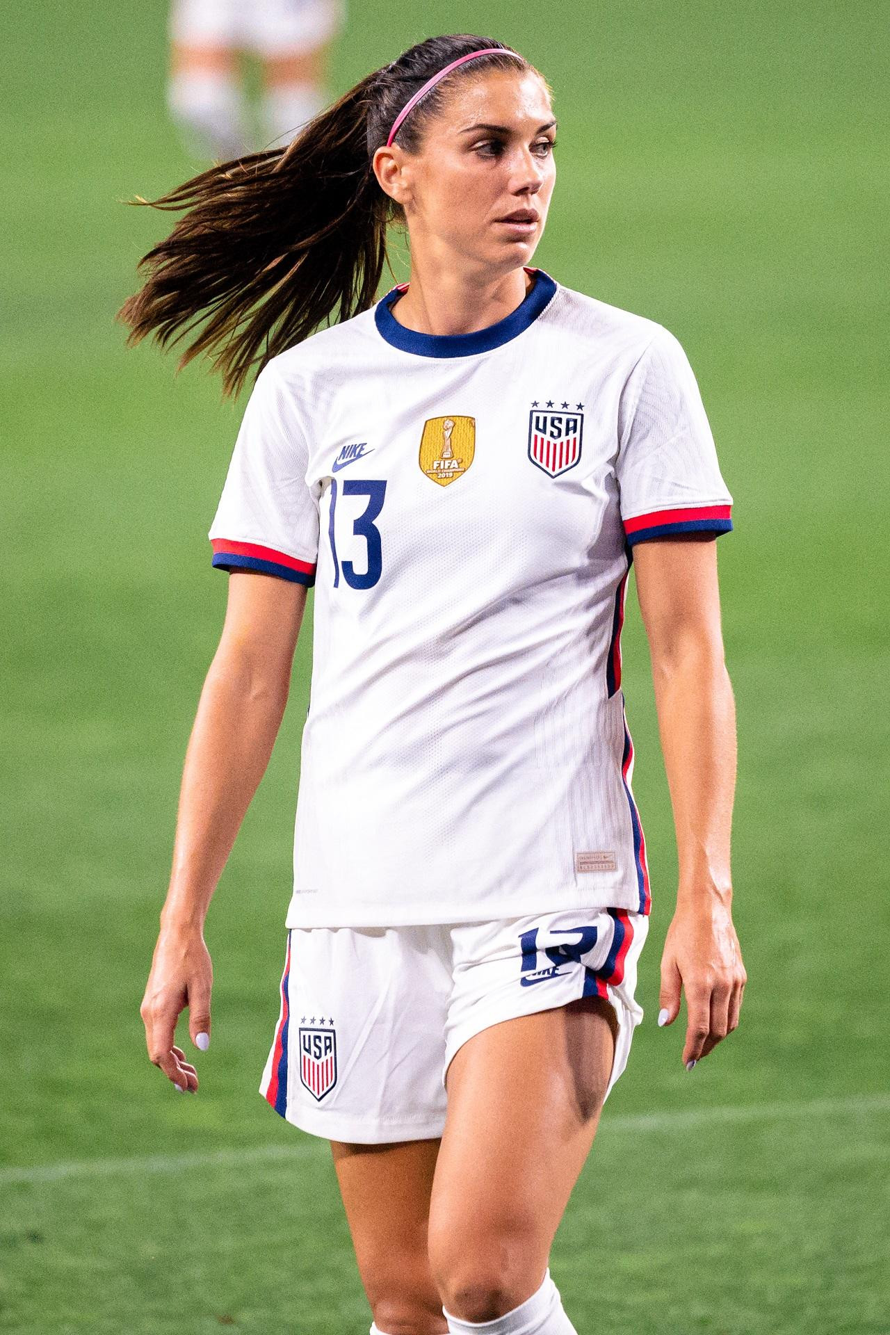 A soccer player in a white team uniform walks on the pitch.