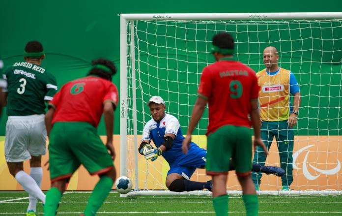 A visually impaired goalkeeper dives to block a shot during a five-a-side football match