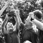 A group of elderly men lifting a trophy after winning a football tournament.