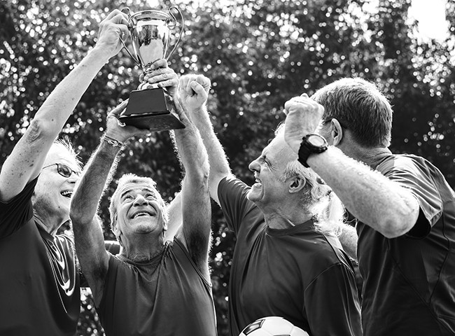 A group of elderly men lifting a trophy after winning a football tournament.