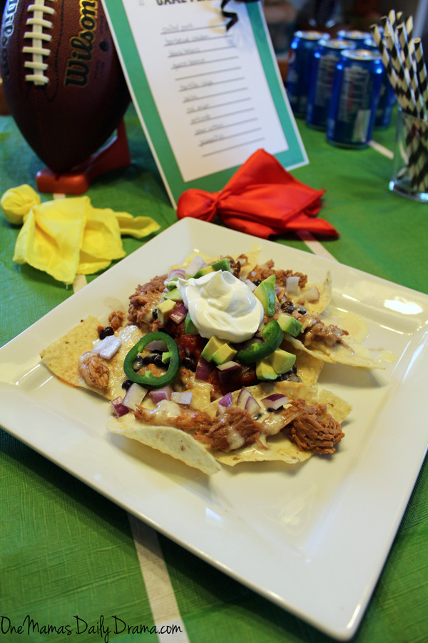 Pepsi pulled pork nachos on a white plate with football party decor in the background