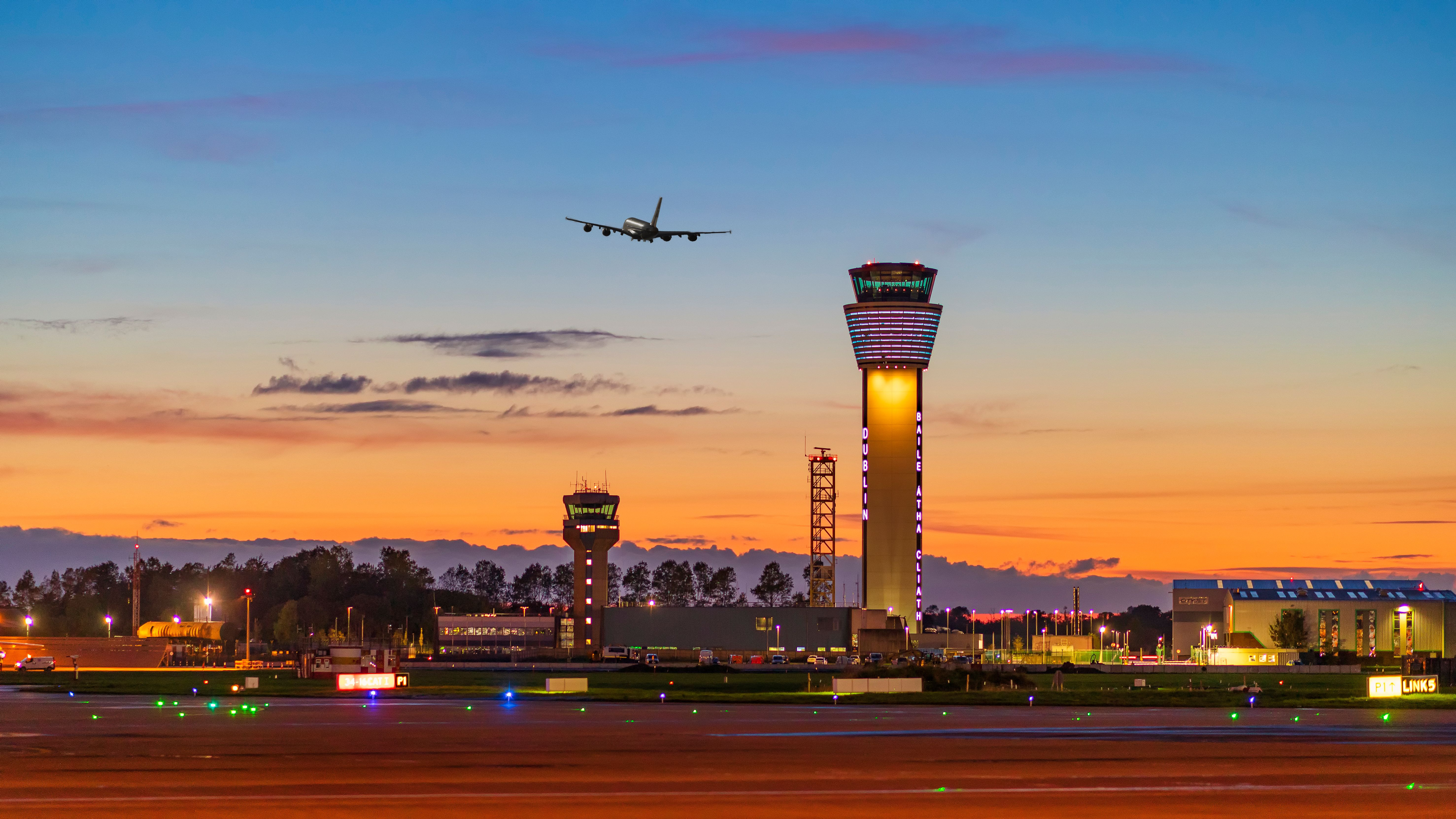 A quad engine aircraft taking off behind a photo of the Dublin Airport Control Tower.