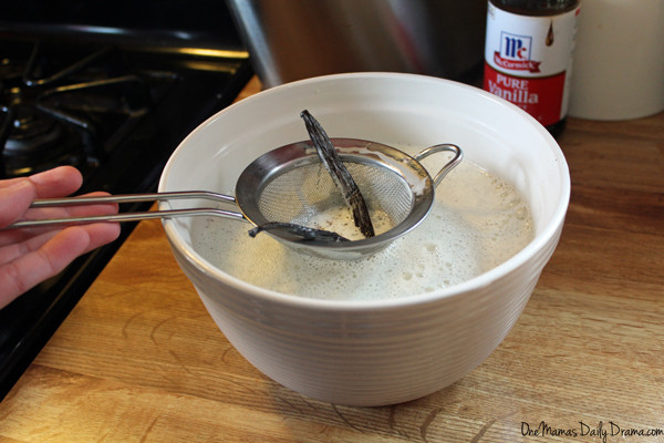 using a strainer to remove the vanilla bean pod from a white bowl full of ice cream mix
