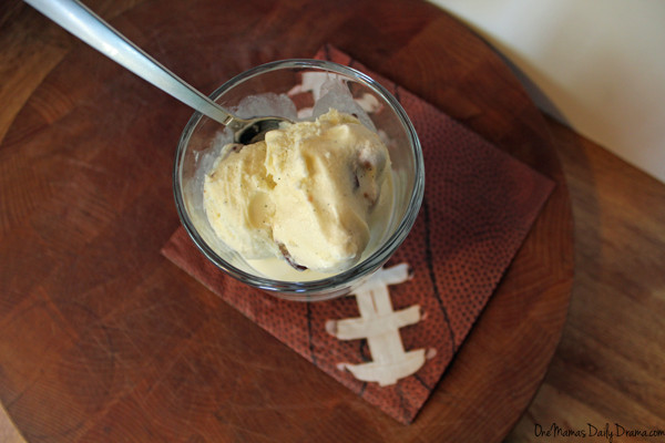 a clear glass cup of snickers ice cream sitting with a football napkin and a wooden cutting board