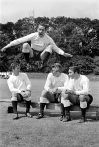 Members of the Tottenham Hotspur team training. Dave Mackay jumping high as teammates sit on the bench talking July 1965. Pic via Mirrorpix.