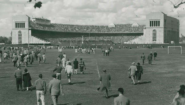 A black and white picture of people walking towards the Shoe, which appears to be full for game day