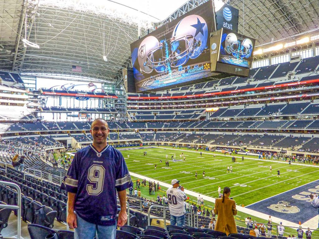 Dan Brewer, of the Ultimate Sports Road Trip blog, stands at his seat in AT&amp;T Stadium for a Cowboys vs Raiders football game on Thanksgiving Day