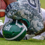 2 teams playing football and one player is falling to the ground and hitting his head while holding the football in his arm