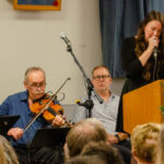 Musicians John Park Wheeler, Brian Hebert and Clint Degarie accompany Bailey Rogers as she sings A Way Down the River at the memorial service for Steve Agnew.